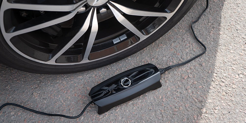 CTEK CS ONE Gen 2 Batterieladegerät während des Ladevorgangs neben einem Autorad auf Asphalt