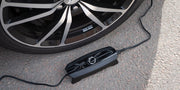 CTEK CS ONE Gen 2 Batterieladegerät während des Ladevorgangs neben einem Autorad auf Asphalt
