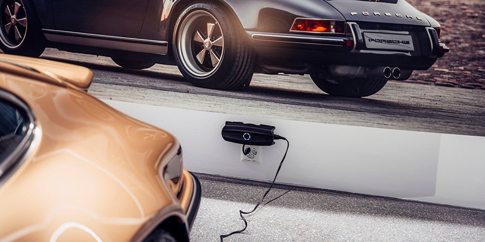 CTEK CS ONE Gen 2 Batterieladegerät in einer Garage neben einem Sportwagen während des Ladevorgangs